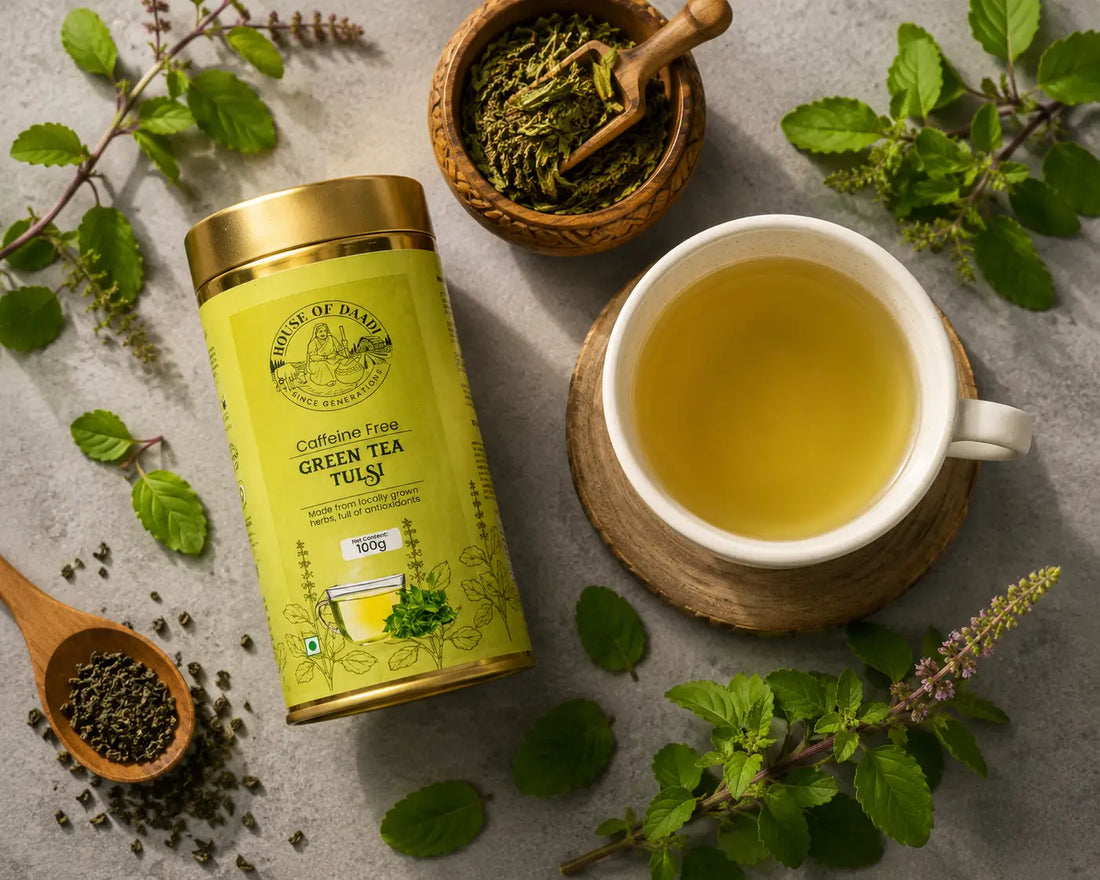 A ceramic cup of freshly brewed Tulsi Green Tea with fresh holy basil leaves, green tea leaves, and a wooden spoon on a light stone surface with soft morning light